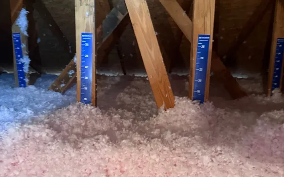 Attic with fresh blown-in insulation and blue depth rulers on the trusses