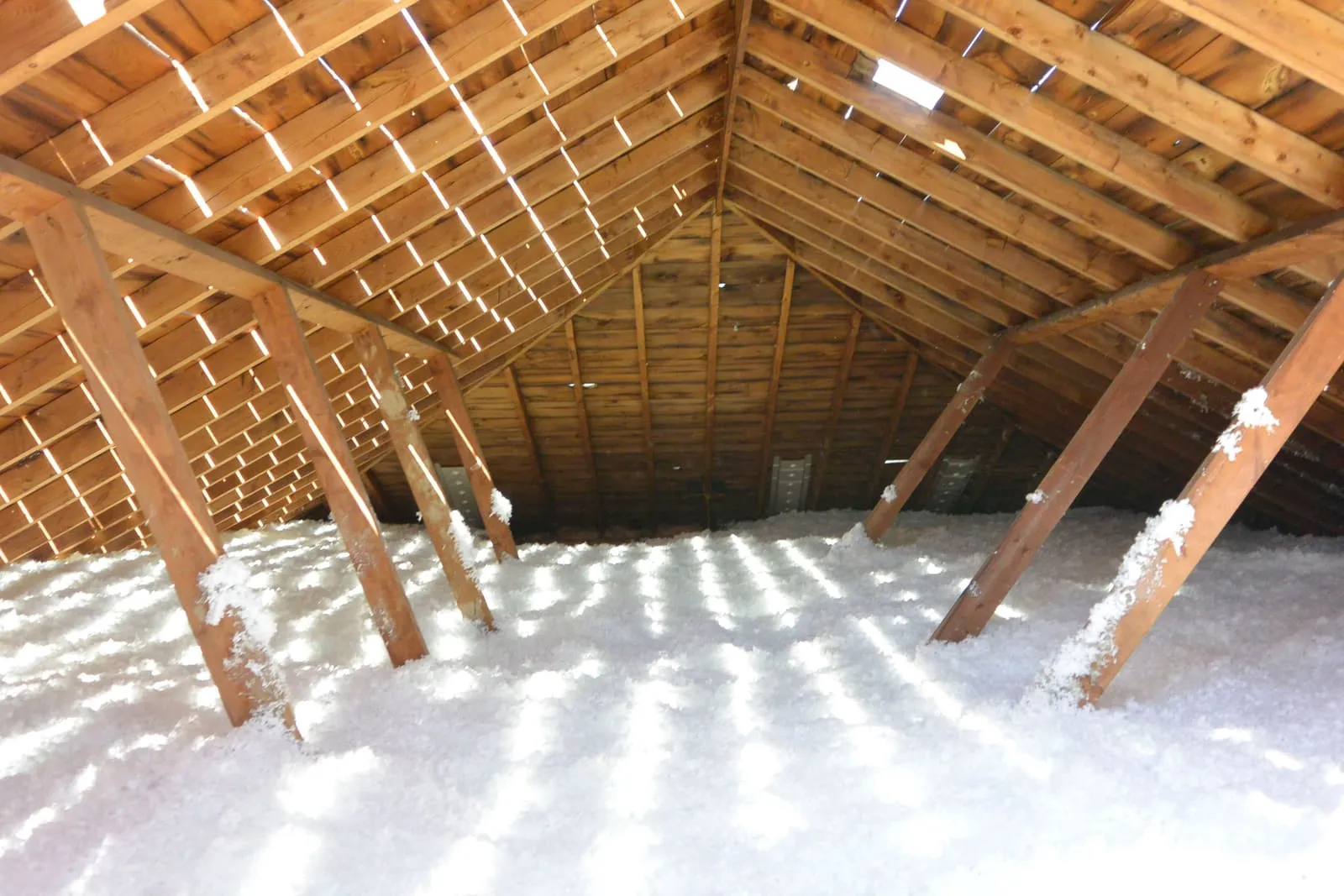 Wooden attic framing covered in a thick layer of blown-in insulation