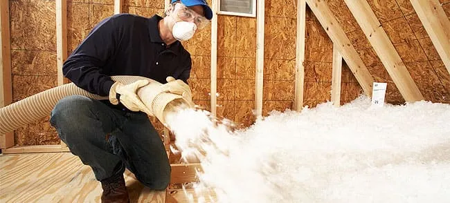Installer in protective gear blowing insulation into an attic