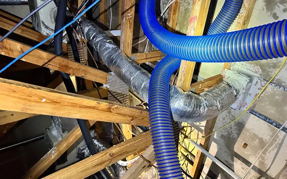 Attic with a vacuum hose and ductwork during insulation removal